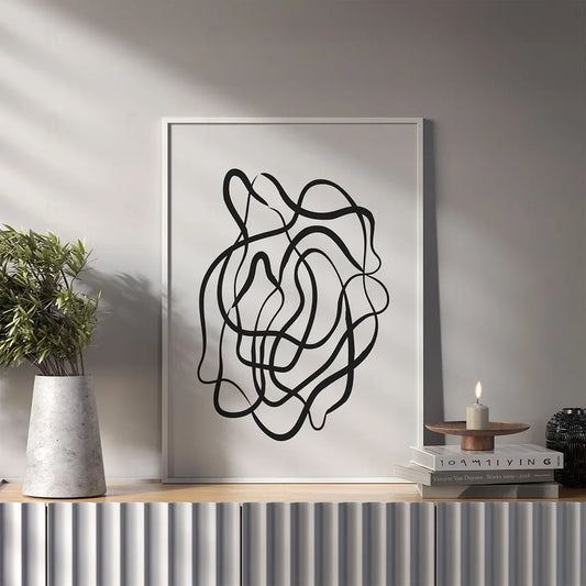 Plakat z czarno-białą, minimalistyczną grafiką przedstawiającą jedną, swobodnie płynącą linię wiszący w salonie