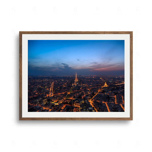 Rozległa panorama Paryża nocą z oświetloną Wieżą Eiffla na tle ciemnoniebieskiego i purpurowego nieba.