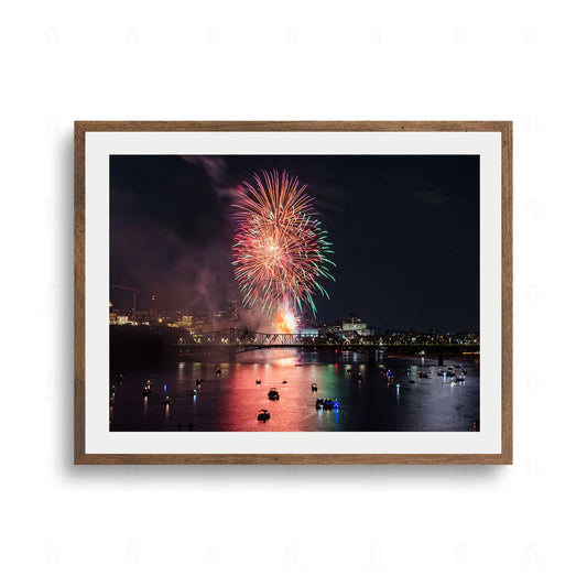 Plakat przedstawiający pokaz kolorowych fajerwerków wybuchających nocą nad rzeką i stalowym mostem. W rzece odbijają się kolorowe światła z łódek.